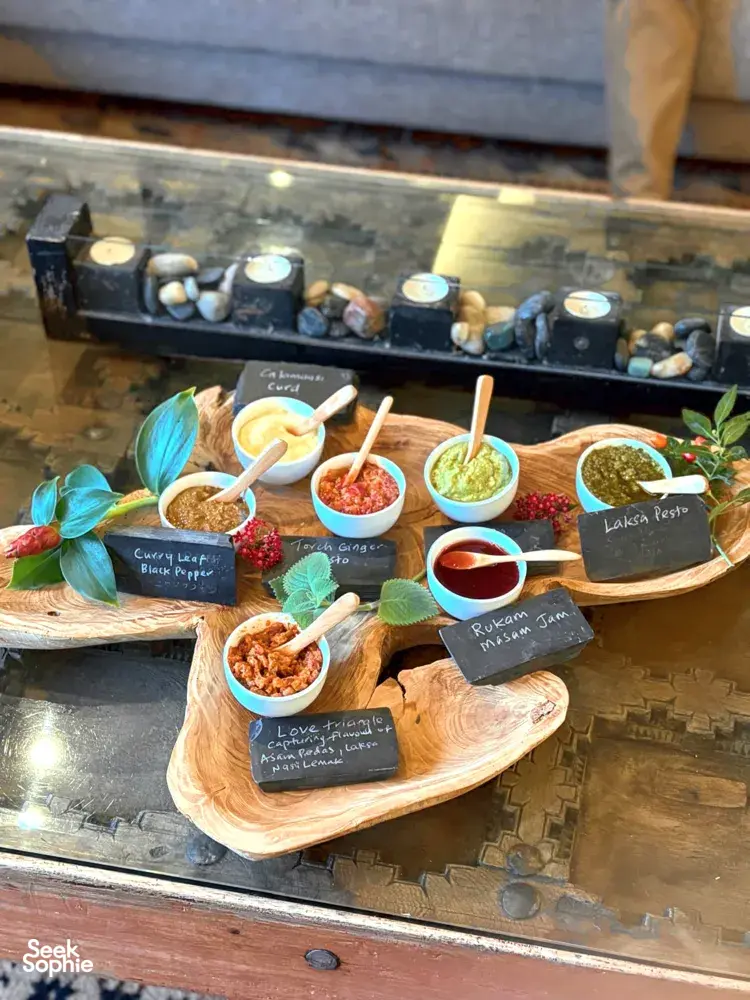 Mangkuk cecah dan sos daripada tumbuhan yang boleh dimakan dengan label kapur di atas papan kayu, disediakan untuk pengalaman membuat roti hidden gems di Singapura