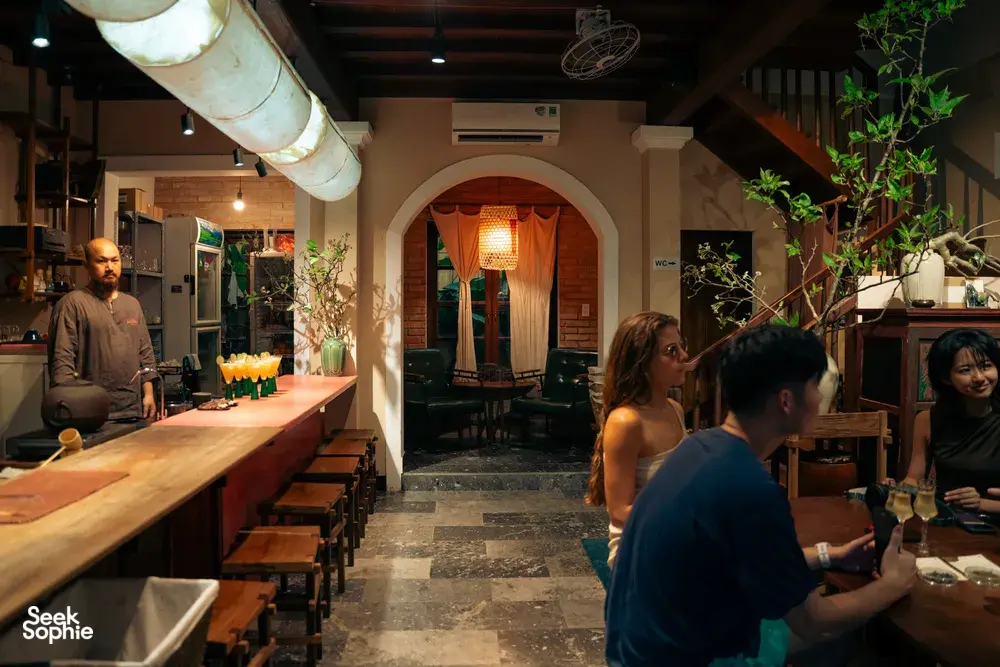 Bartender menyediakan minuman di sudut bar berdinding bata yang nyaman sambil para tetamu menikmati lawatan koktel Hoi An