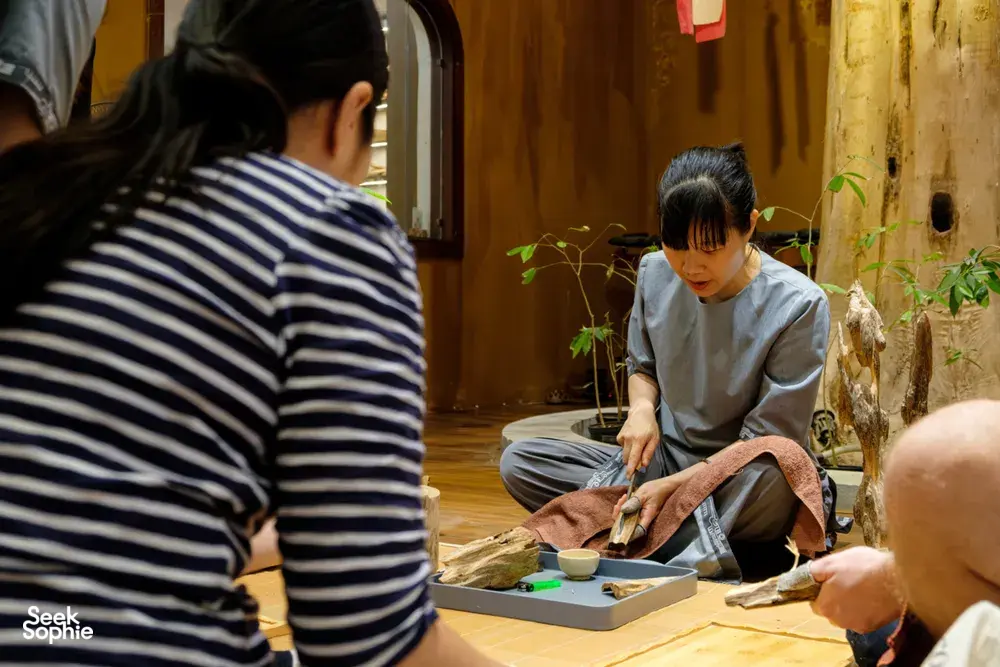 Woman inspects and trims agarwood wood on a workshop table in Hanoi during an Up Travel Vietnam rare agarwood tour
