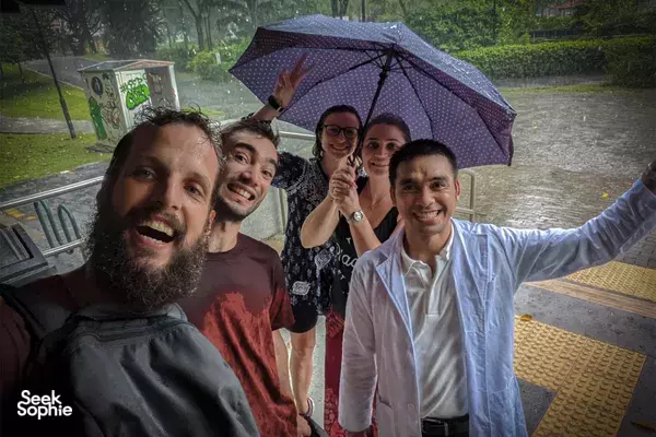 Group of participants smile under an umbrella during a rainy outdoor sustainability scavenger hunt in Singapore