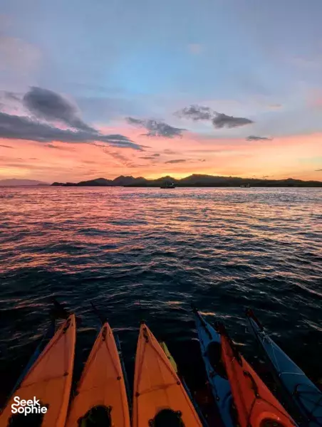 Sunset kayak trip in Labuan Bajo with orange kayaks on calm water, silhouetted islands and clouds over the horizon