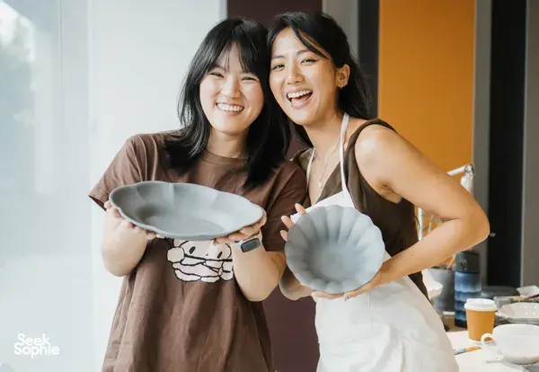 Two workshop participants at Ina Atelier in Singapore smile while holding handmade European-style ceramic plates — workshops in Singapore