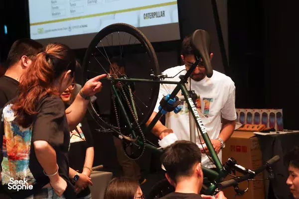 Unspokin bicycle workshop: a guide and participant adjust a green bike frame in the class room during the build, workshops in Singapore