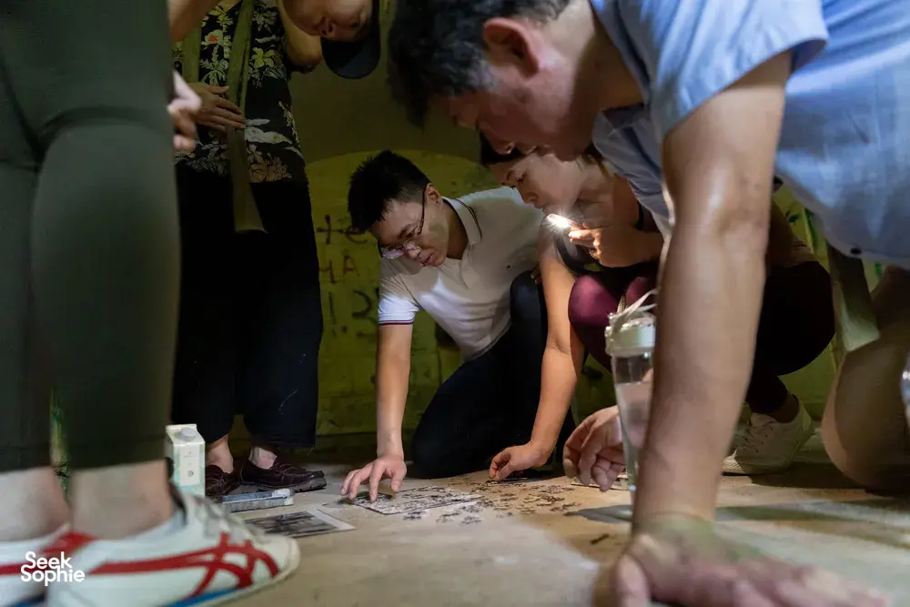 People huddled over a map and cards by lantern light, solving clues during Fort Serapong discovery adventure in Singapore
