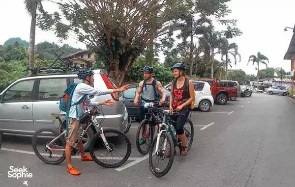 Cyclists in helmets pause with their bikes by the roadside in Kuching, set for a Paradesa Borneo jungle cycling outing