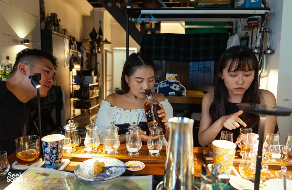 Glasses of small-batch whisky on a candlelit table as guests taste in a host-led hidden home bar in Katong, Singapore together