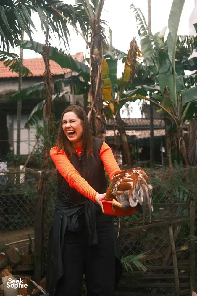 Smiling woman holding a large clay bowl among palms and greenery at a workshop in Hoi An’s countryside at dawn