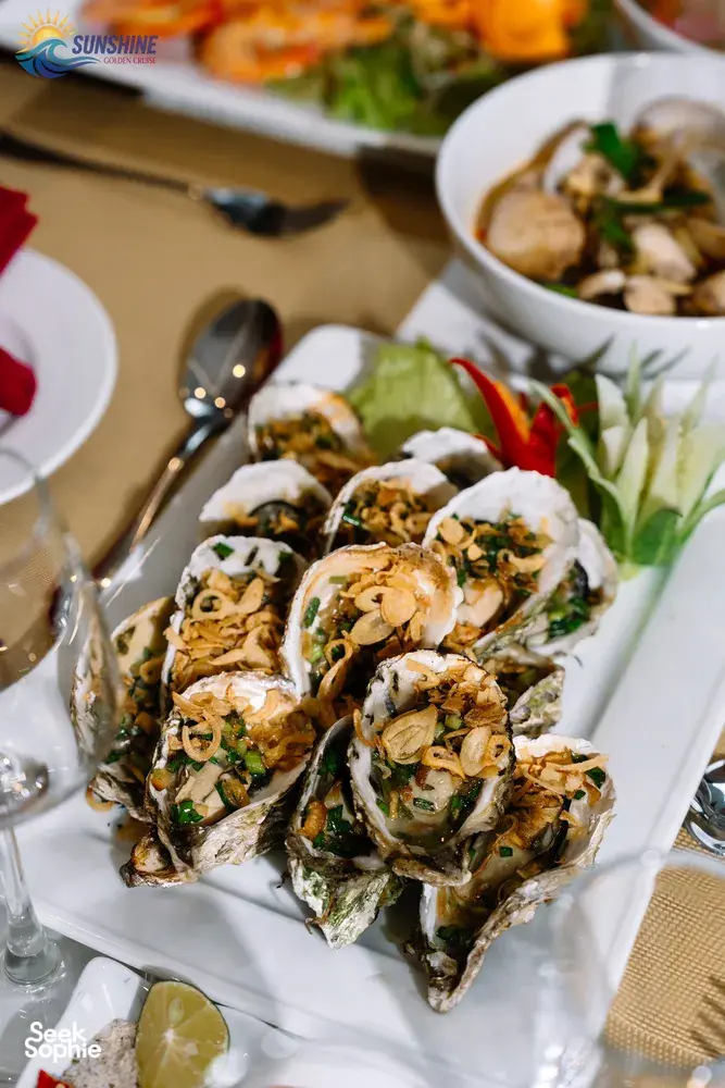 Grilled shellfish appetisers with herbs on white plates, served as part of dinner aboard a luxe 2D1N Cat Ba cruise