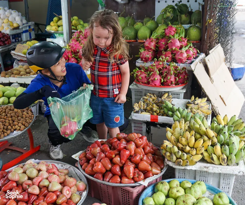 Children browse a local produce market on Mekong Island, with bowls of dragon fruit, limes and tomatoes in front of them near Ho Chi Minh City
