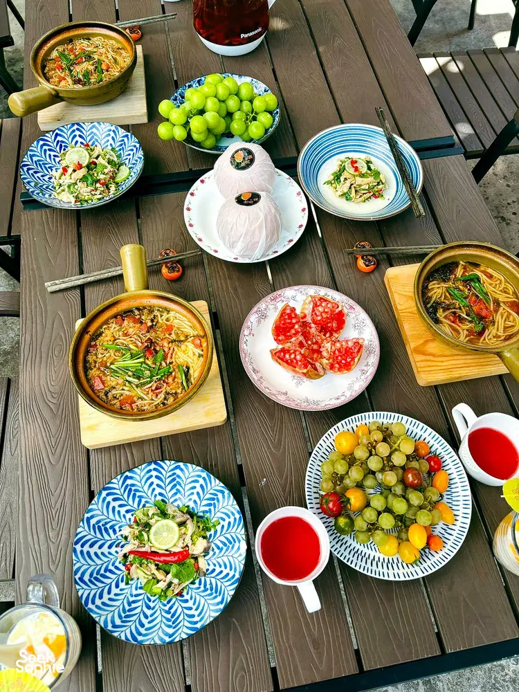 Top-down view of a Lijiang table spread with Yunnan noodles, appetisers and fresh fruit after cooking together