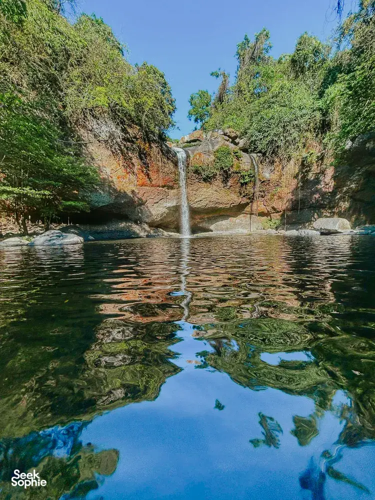 Wide view of a waterfall dropping into a calm pool surrounded by trees in Khao Yai National Park outdoors