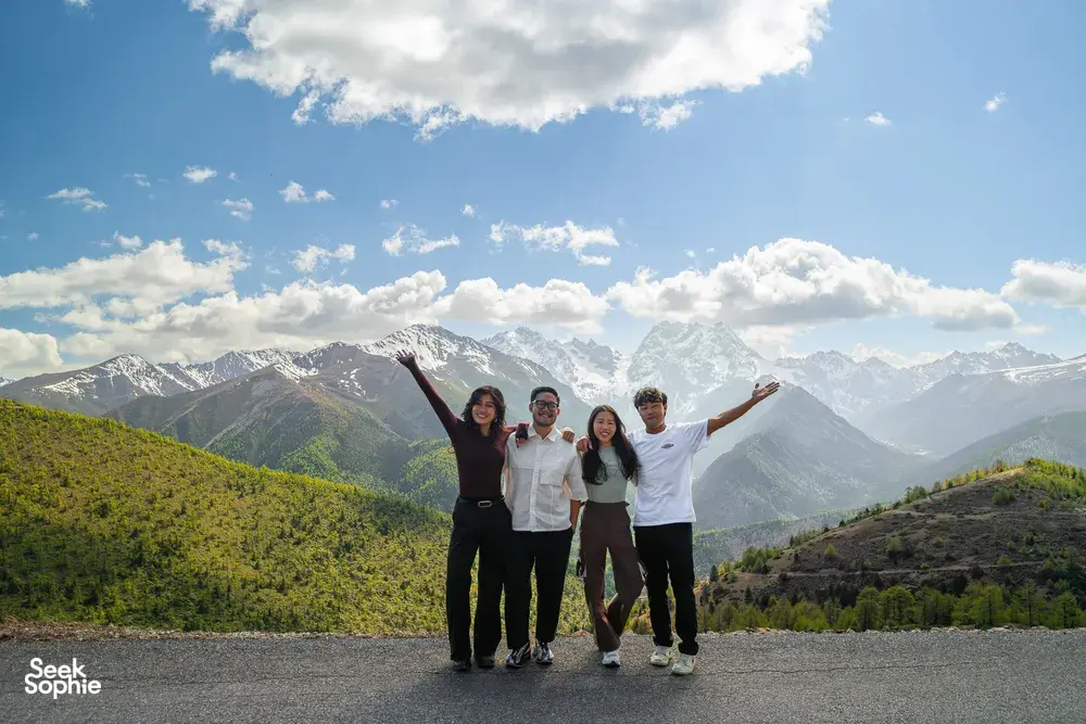 Travellers with a Tibetan guide posing on a mountain road with snowy peaks above Shangri-La during a 6-day loop trek