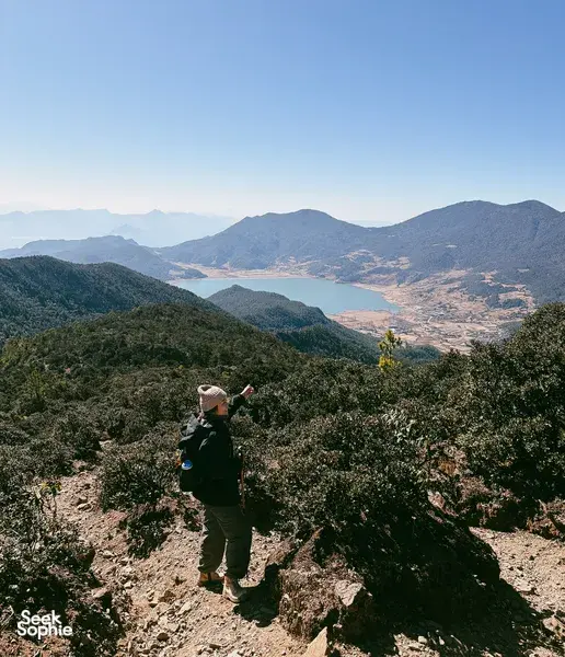 Hiker on a rocky ridge overlooking Jade Dragon Snow Mountain and a mountain valley lake on a guided hike in Lijiang