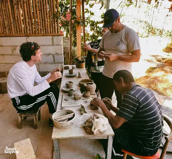 Small group learning pottery at a shared work table as an instructor demonstrates clay techniques in Dali’s ancient village