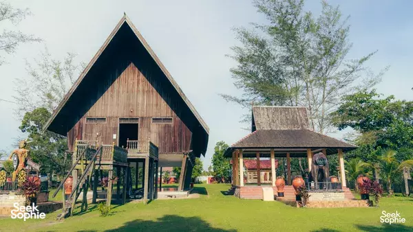 Traditional wooden houses in a grassy compound with carved statues at the entrance in Pangkalan Bun, Tanjung Puting