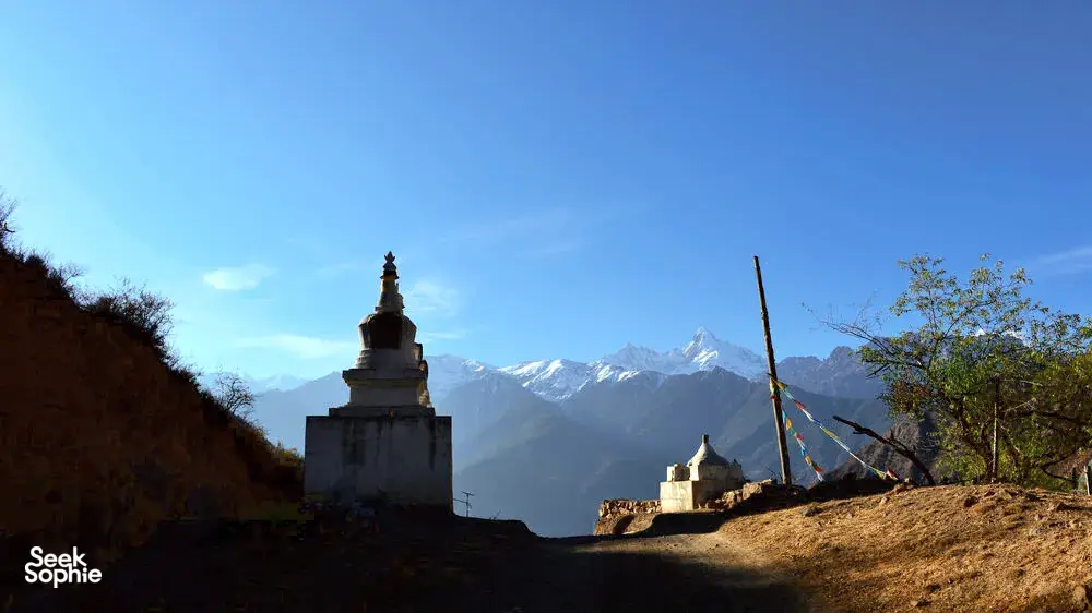 Tibetan stupa shrine on a hilltop with Meili Snow Mountain peaks in the distance beneath a clear blue sky