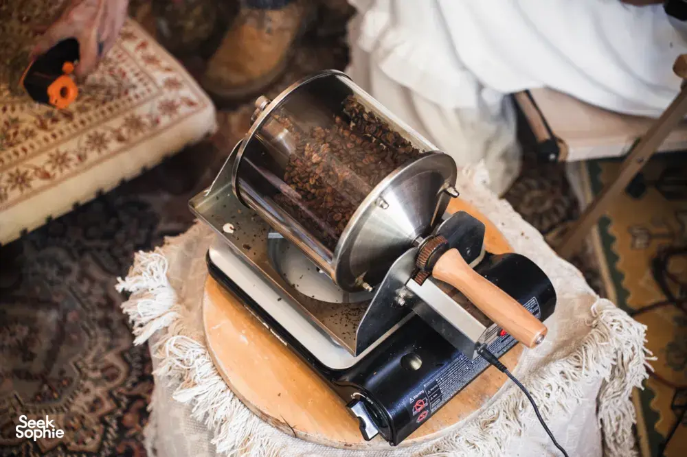Metal coffee roaster set on a cloth-covered table for roasting, with beans visible during a hands-on coffee brunch — workshops in Singapore