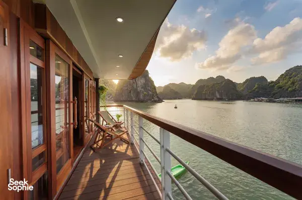 Sunlit wooden cruise balcony with lounge chairs and balcony rail, overlooking calm karst waters on a boutique cruise in Cat Ba