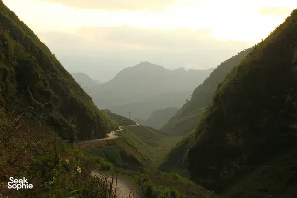 Misty mountain valley at sunrise with a winding track through green hills and distant ridges in China