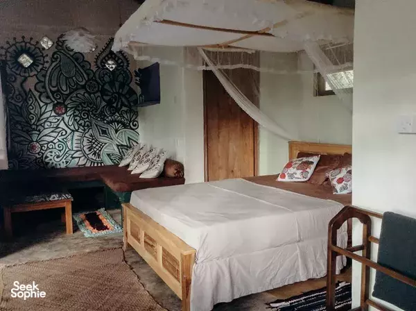 Canopy bed in a Sri Lanka guest room with patterned wall decor and open doorway, pillows neatly arranged on the bed