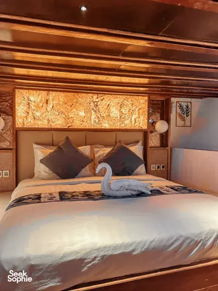 Deluxe phinisi cabin bedroom in Labuan Bajo with made bed, pillows and a folded towel, designed for a restful Komodo Island cruise