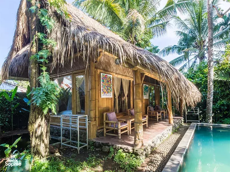 Thatched-roof bamboo cabana beside a turquoise swimming pool surrounded by lush tropical plants at Omunity Bali in Bali