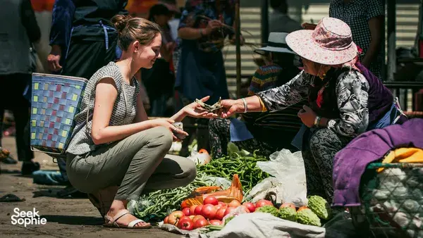 Local market visit in Xizhou Old Town, Dali, as a visitor selects fresh vegetables with a vendor at a bustling stall