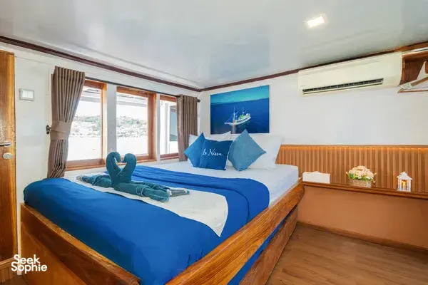 La Famille cabin on a Komodo boat with folded towel swan on blue bedding and sea view through the windows, Labuan Bajo