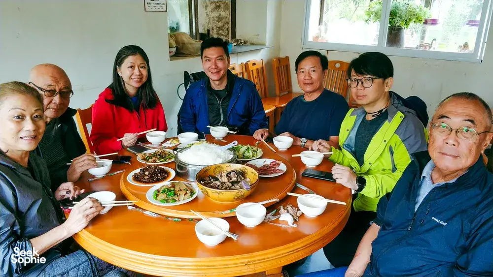 Communal lunch at a round table with bowls and chopsticks indoors during a countryside trek with The Bivou Lijiang in Lijiang