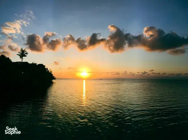 Sunset over calm ocean with a warm sun reflecting on the water and palm-lined coast seen from Semporna
