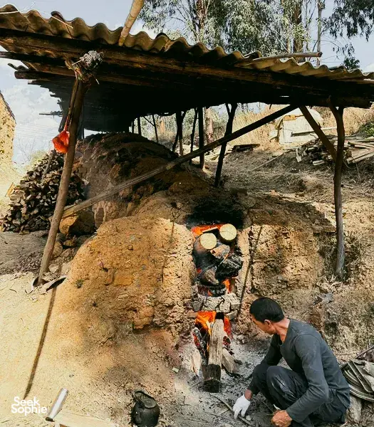 Jay kneading clay beside an earthen kiln at a traditional pottery village workshop in Dali day trip with Discovery More
