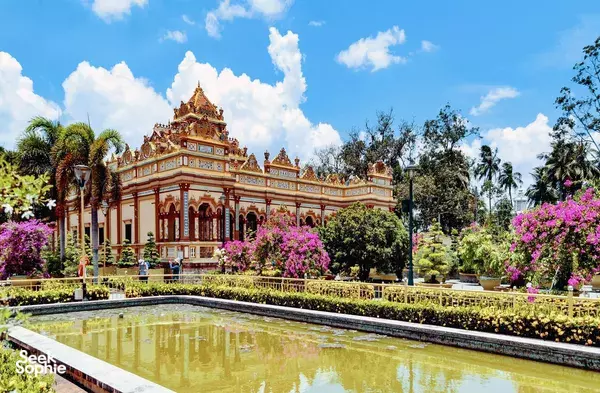 Ornate gold-and-cream temple building in a landscaped garden beside a still pond in Ho Chi Minh City, Vietnam