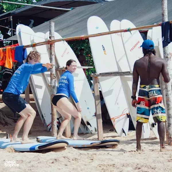 Beginner surf boards staged under a shade canopy on Weligama beach, as instructors help students prepare for their session