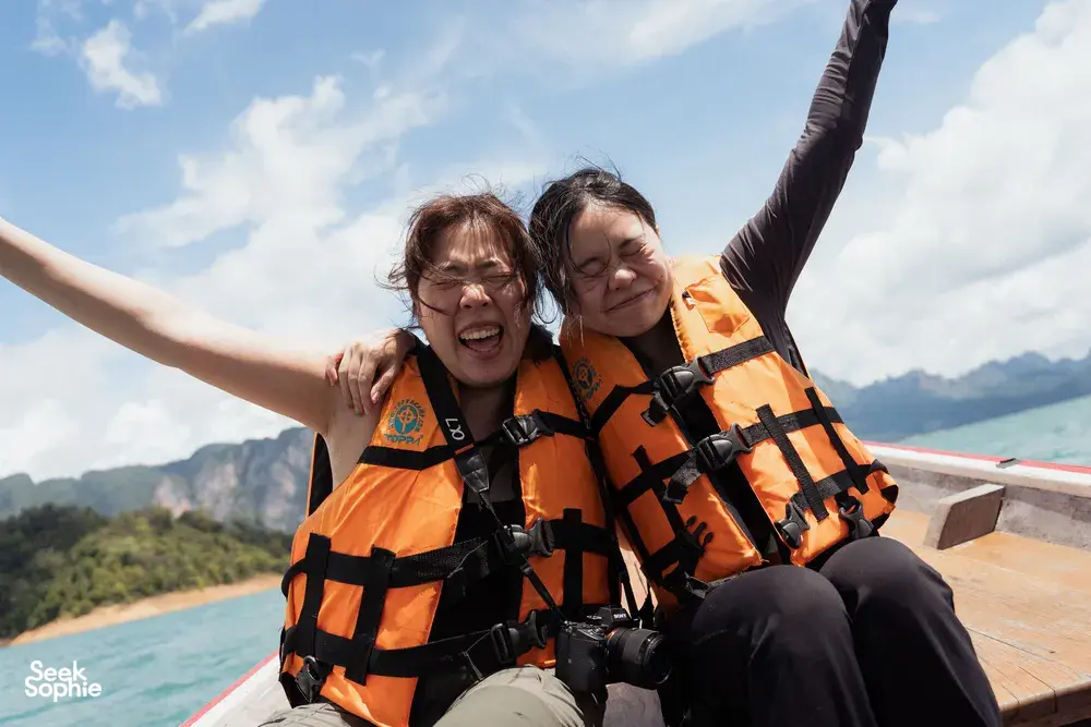 Two guests in orange life jackets grin on the boat deck during a private day trip, heading across open water on Cheow Lan Lake