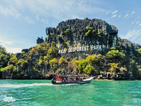 Tour boat on turquoise water passing the Kilim Geoforest Park cliffs during a mangrove cruise in Langkawi