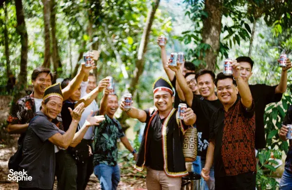 Sekumpulan jiran dan pengembara tersenyum sambil mengangkat minuman di ruang luar Ngapuh Homestead di hutan hujan Kuching