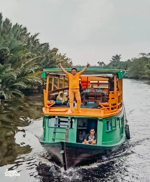 Klotok boat cruising the river in Tanjung Puting, Pangkalan Bun, with travellers on deck during an orangutan adventure