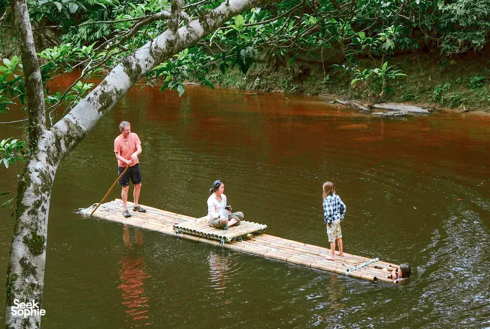 Guests enjoying bamboo rafts on a shaded river during a regenerative homestead stay on Bidayuh ancestral land near Kuching