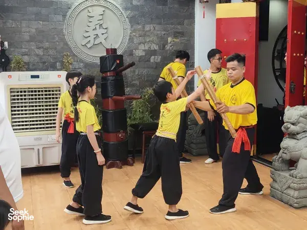 Group practising kung fu steps near lion-dance prop drums inside a Ho Chi Minh City Chinatown training room