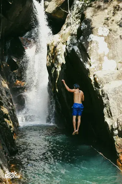 Nguyen Tours Hoi An secret waterfall stop on a motorbike adventure, a swimmer jumping into a turquoise pool by the falls