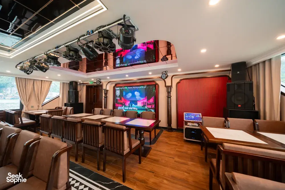 Dining and lounge area on a luxe Cat Ba cruise, with set tables, lounge seating, and a large TV entertainment screen