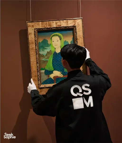 A guide from Quang San Art Museum adjusts a framed Vietnamese portrait for visitors during an art tour in Ho Chi Minh City