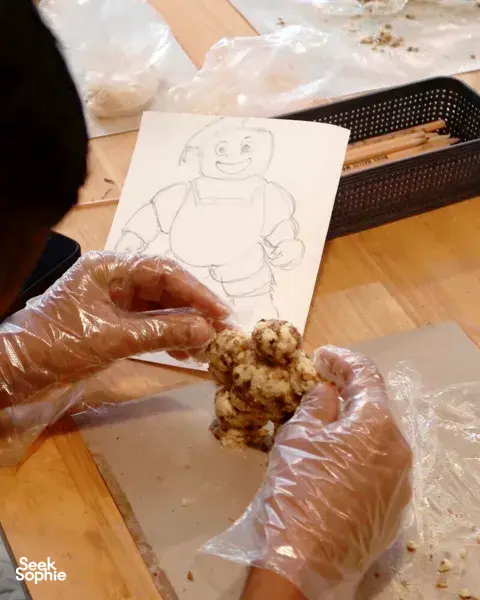 Gloved hands rolling butter mixture beside a sketch on paper during a butter crafting workshop in Singapore for workshops in Singapore