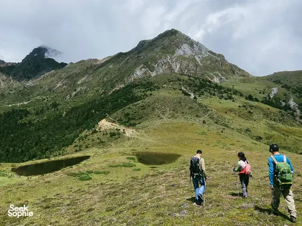 Small group hiking with backpacks on Jade Dragon Snow Mountain near Lijiang, overlooking a green valley and peak