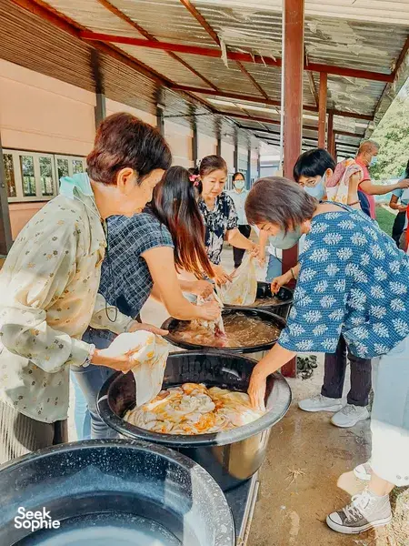 People working around large outdoor dye tubs and fabrics in a covered hall during Dip-Dye By Noo’s eco-print jamming near Chiang Mai