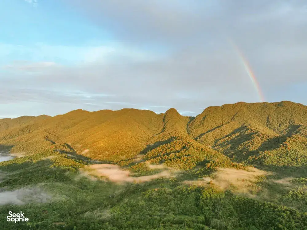 A rainbow arcs over green ridges and a winding river in the rainforest valley near Ngapuh Homestead, Kuching