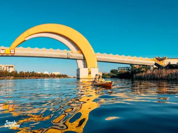 Kayaks gliding under a yellow bridge at sunset on a Hoi An Kayak Tour in Hoi An, with warm reflections on the water