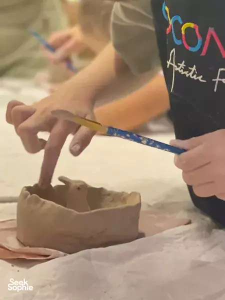 Hands painting and shaping a clay bowl during a kids pottery class in Singapore, with brushes and a pottery rim — workshops in Singapore