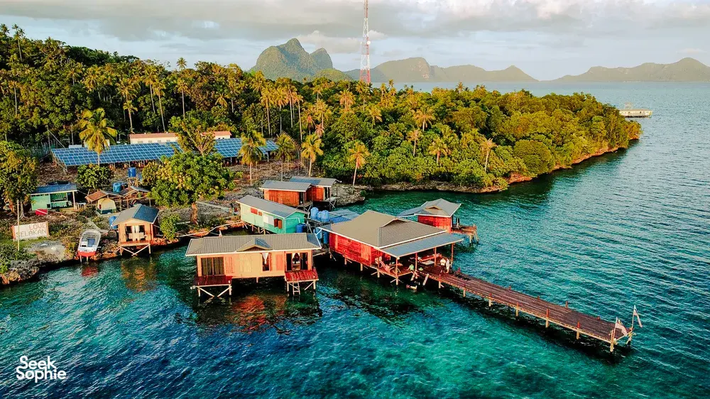 Aerial view of Luma Selakan sea lodge complex in Semporna with wooden platforms, boatsheds and jetty over the lagoon