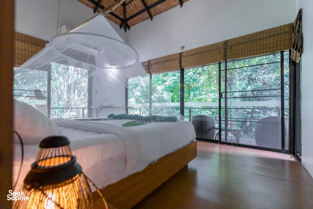 Sheer-canopy bed inside Anurak Lodge at Khao Sok National Park, with open windows framing the surrounding rainforest